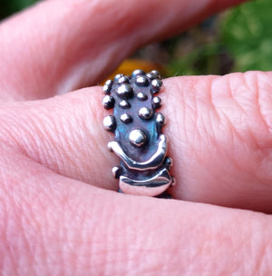 Finger wearing blackened sterling silver Bubble Ring with a buckle effect pattern and little bubble decorations. Designed and handmade in Ireland.