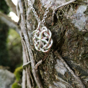 A close up of the Celtic Knot Pendant, made in Ireland. This celtic knot jewelry piece is hanging beautifully from a tree at Irish Jewellery Designer Elena Brennan's studio.