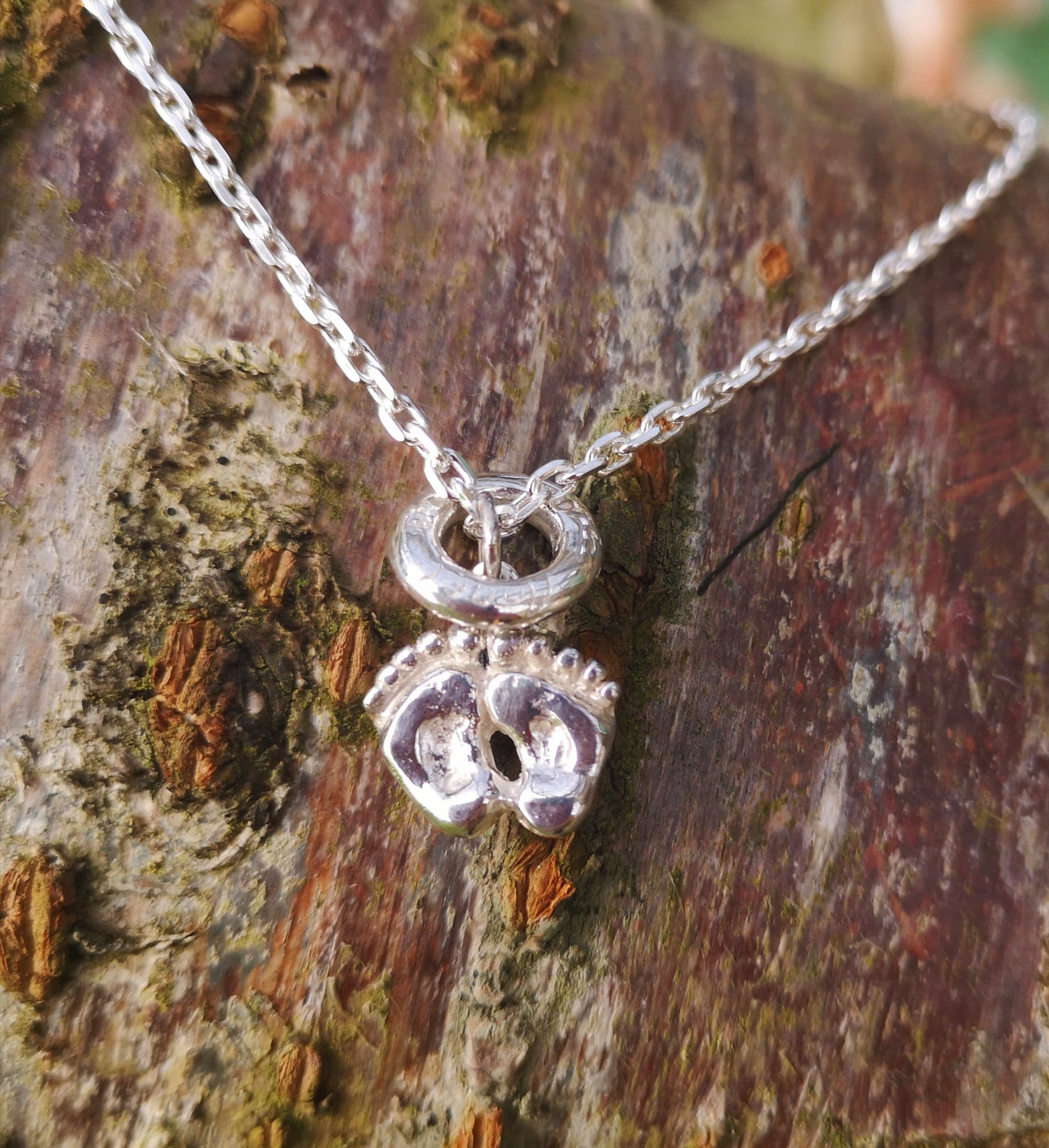 Sterling silver baby feet and halo pendant, part of Elena Brennan's angel jewelry collection. Photographed here against tree bark.