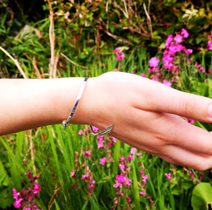 The Irish sterling silver Earth Angel Feather Bangle looks delicate and fits comfortably on your wrist, photographed in nature setting