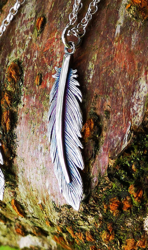 A close up of the Irish Sterling Silver Earth Angel Feather Pendant, photographed against tree bark