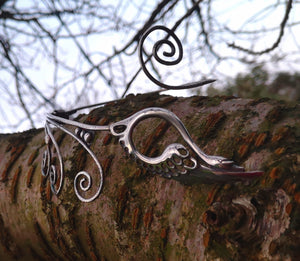 Children of Lir sterling silver torc necklace, featuring a Celtic swan. This torc jewelry piece is sitting on a tree branch