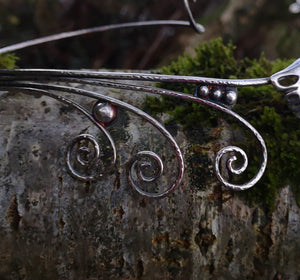 Detail of the Children of Lir sterling silver torc necklace, featuring a Celtic swan. This torc jewelry piece is sitting on a tree branch