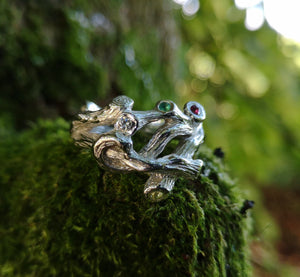 A sterling silver family birthstones ring in the shape of twigs that can also function as an Irish wedding ring or promise ring. The ring is sitting on a mossy surface.
