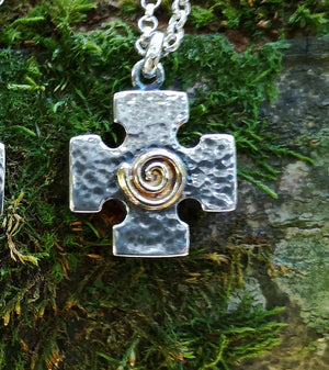 Detail of the Crux Quadrata, a Greek cross pendant with a gold spiral at the centre, hanging against mossy tree bark. Handmade in Ireland.