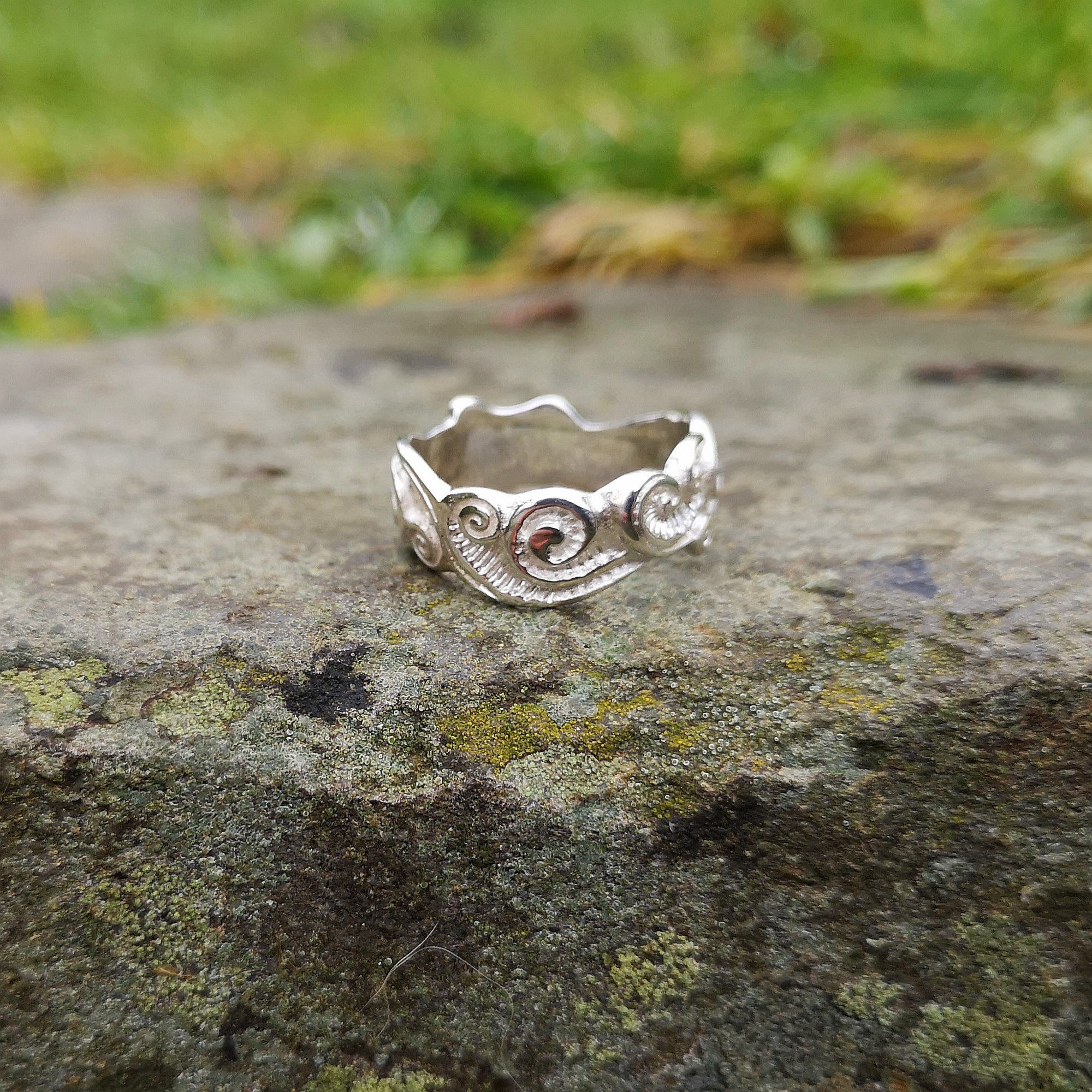 The sterling silver Celtic Spirals Wedding Ring perched on a smooth rock outside. This Irish wedding ring is handmade in Ireland by Elena Brennan.