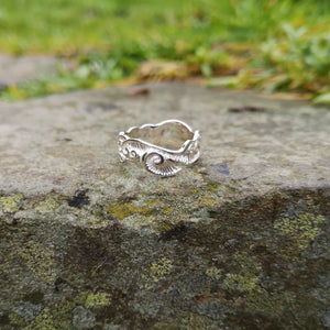This sterling silver Irish wedding ring is perched on a smooth rock. Decorated with Celtic spirals, it is handmade in Ireland by Elena Brennan.