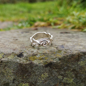 The sterling silver Celtic Spirals Wedding Ring perched on a smooth rock outside. This Irish wedding ring is handmade in Ireland by Elena Brennan.