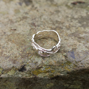 Close up of the sterling silver Celtic Spirals Wedding Ring, perched on a smooth rock. This Irish wedding ring is handmade in Ireland by Elena Brennan.