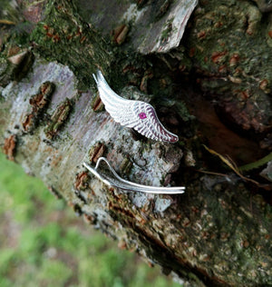 Handmade sterling silver Angel Wings Ear Cuff earrings with red gemstone set in the middle, displayed on tree bark. Part of Elena Brennan's Irish My Angel jewelry collection.
