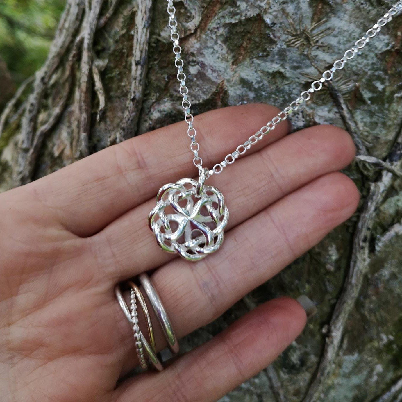 The Celtic Love Knot pendant is handmade from sterling silver and crafted in Ireland. This Celtic knot jewelry piece is perched against tree bark
