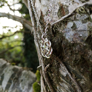 A side view of the handmade Celtic knot jewelry piece hanging from a tree.  The Celtic Love Knot Pendant was made by Irish Jewellery Designer Elena Brennan.