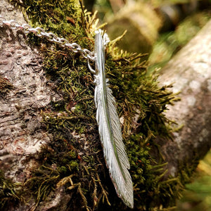 The sterling silver Earth Angel Feather Pendant at a closer angle to show sizing of the delicate unique pendant, photographed against tree bark