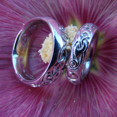 Matching celtic style wedding rings sitting on a pink flower.