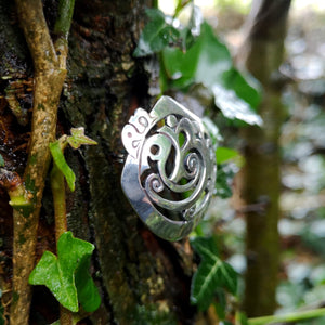 Cavan (An Cabhán) Brooch made of sterling silver, sitting on tree bark. Its Celtic designs is inspired by the landscape of County Cavan.