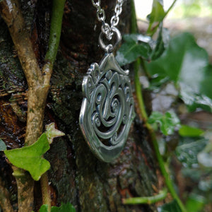 Side view of the Cavan 'An Cabhán' pendant made of sterling silver hanging against tree bark.