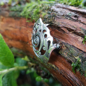 Detail of the Cavan (An Cabhán) Brooch made of sterling silver, sitting on tree bark. Its Celtic designs is inspired by the landscape of County Cavan.