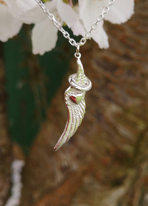 The angel wing and halo pendant hanging from a tree branch and a white flower behind it. This angel jewellery is handmade in Ireland.