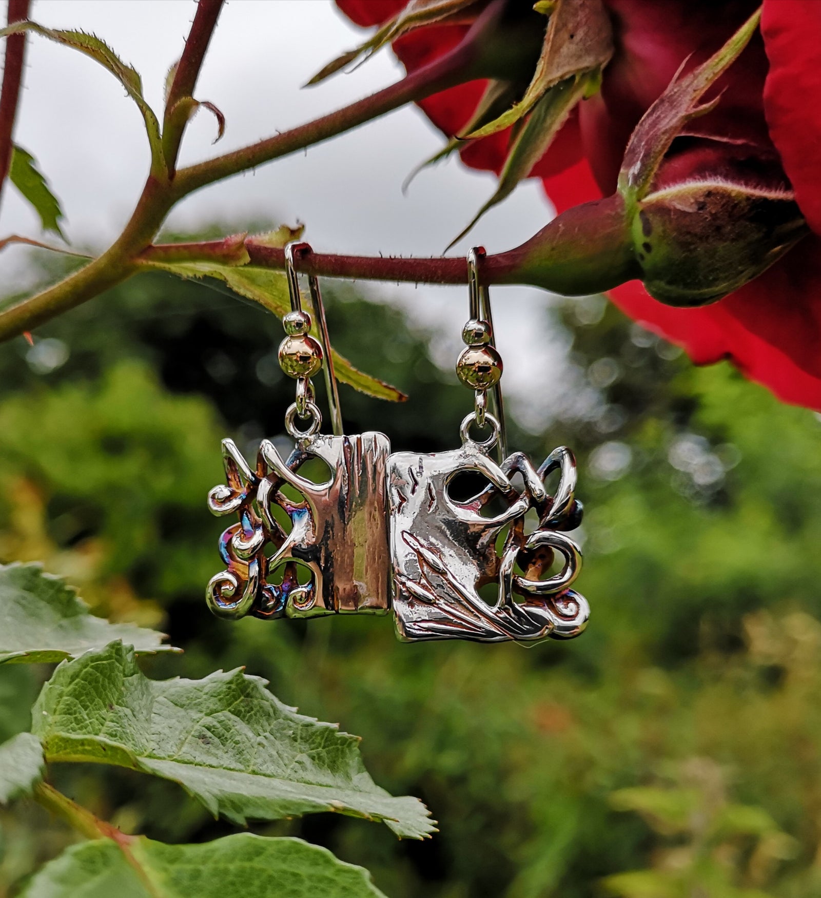 The handmade Bog Book Small Page Drop Earrings hanging from a flower.