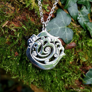 The Cavan 'An Cabhán' pendant made of sterling silver is hanging against mossy tree bark.