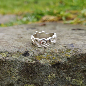 The sterling silver Celtic Spirals Wedding Ring is an Irish wedding ring and is perched on a smooth rock outside. Handmade in Cavan, Ireland.