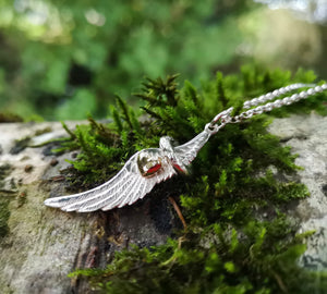 Close up of the sterling silver angel wing and halo with gold heart pendant sitting on a mossy tree branch. This angel jewellery piece is handmade in Ireland.
