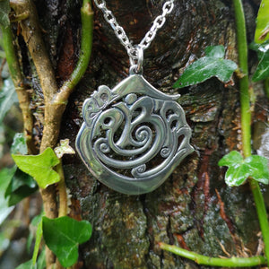 The Cavan 'An Cabhán' pendant made of sterling silver is hanging against tree bark.
