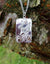 Dancing at the crossroads silver pendant with gold music note, hanging against tree bark.