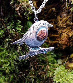 Detail of the Robin Red Breast Pendant or An Spideog, hanging against tree moss.