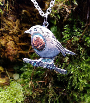Detail of the Robin Red Breast Pendant or An Spideog, hanging against tree moss.