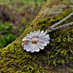 This Dog Daisy pendant is made of sterling silver and gold and is sitting on a mossy tree branch. Daisy Jewellery handmade in Ireland by Elena Brennan.