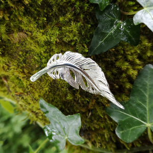 Silver angel feather brooch sitting on ivy covered mossy tree bark. Part of the My angel jewellery collection, made in Cavan.