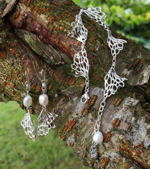 Gossamer wave silver and pearl earrings and bracelet sitting on a branch.