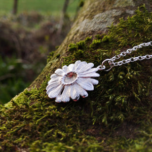 This Dog Daisy pendant is made of sterling silver and gold and is sitting on a mossy tree branch. Daisy Jewellery handmade in Ireland by Elena Brennan.