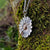 This Dog Daisy pendant is made of sterling silver and gold and is hanging from a mossy tree branch. Daisy Jewellery handmade in Ireland by Elena Brennan.