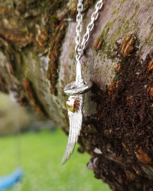 The angel wing and halo pendant hanging from a tree branch. This angel jewellery is handmade in Ireland.