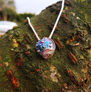 Journey of Life medium size pendant with blue sheen hanging on tree branch. Handmade in Cavan, Ireland.