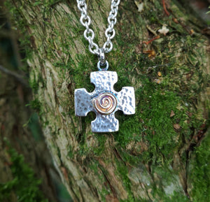 The Crux Quadrata, a Greek cross pendant with a gold spiral at the centre, hanging against mossy tree bark. Handmade in Ireland.