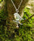 Detail of the Robin Red Breast Pendant or An Spideog, with a gold heart charm. It is hanging from a tree branch.