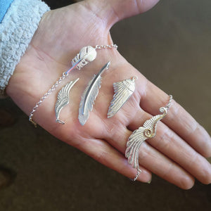 The "Cherish" Baby Angel Feather Bracelet from Elena Brennan's 'My Angel' collection, is made from Irish Sterling Silver. It is displayed on the left of the hand alongside other sterling silver angel jewellery pieces