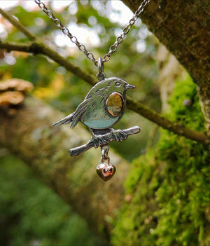 Detail of the Robin Red Breast Pendant or An Spideog, with a gold heart. It is hanging from a tree branch.