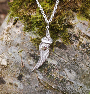 The angel wing and halo pendant is hanging against mossy tree bark. This angel jewellery is handmade in Ireland.