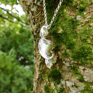 The Mara pendant, made of twisted sterling silver with a spiralling motion hanging against tree bark. Bespoke jewellery made in Ireland.