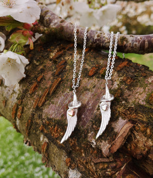 Two angel wing and halp pendants hanging from a tree branch. Part of the My Angel jewellery collection.