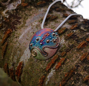 Cúrsa an tSaoil pendant hanging on a tree branch. Handmade jewellery from Cavan, Ireland.