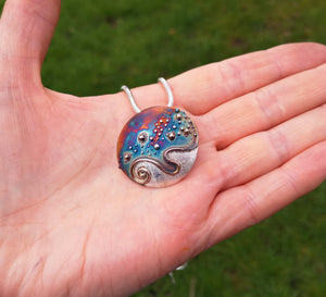 A hand holding the silver Cúrsa an tSaoil pendant, handmade in Ireland.
