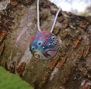 Cúrsa an tSaoil pendant hanging on a tree branch. Handmade jewellery from Cavan, Ireland.